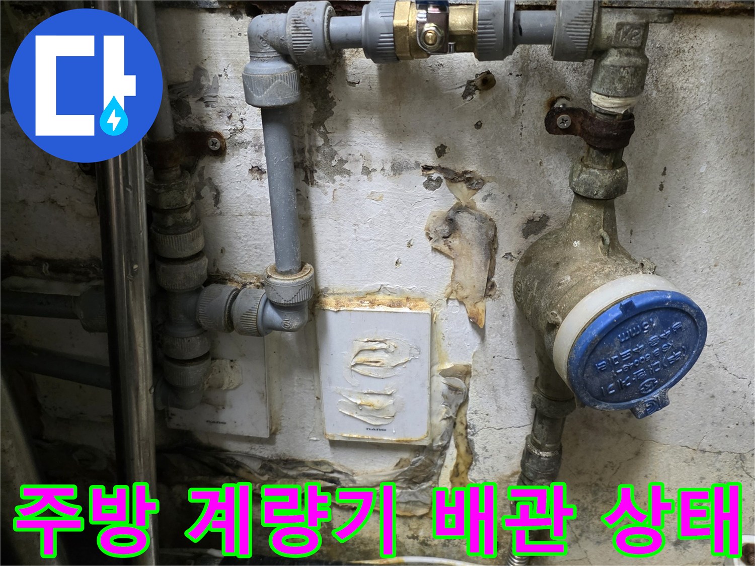 식당 주방 벽면에 설치된 수도 계량기와 노출된 배관의 모습입니다.