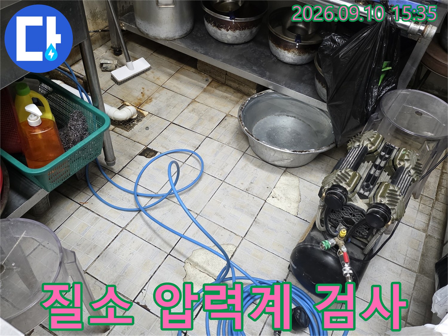 주방 바닥 타일 위 파란색 호스와 배관 압력 측정 장비