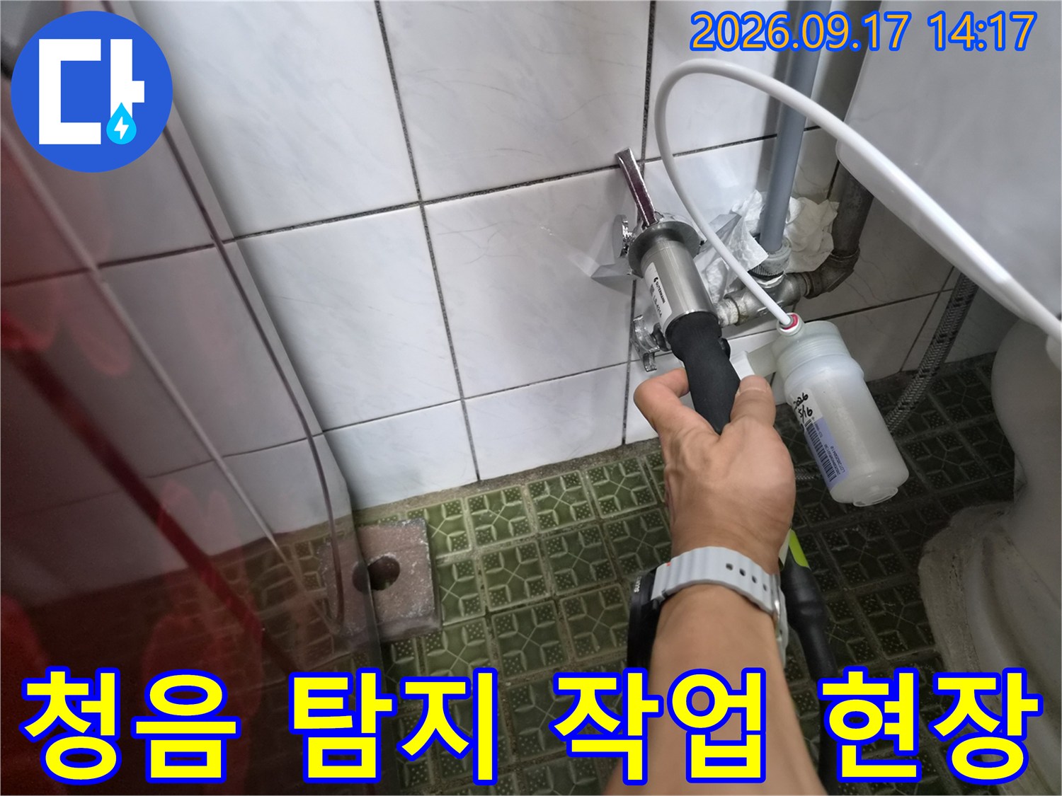 변기 밸브 주변 배관을 - 청음 장비로 면밀히 조사하고 있는 장면입니다.